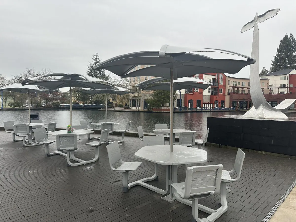 Outdoor patio with white tables, umbrellas, and a waterfront view with a modern sculpture at Lee's Kitchen，a Chinese Restaurant in Tualatin